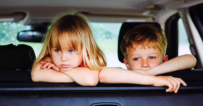Sad children looking out the back window of a car