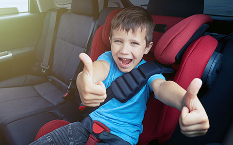 Boy in car back seat with thumbs up