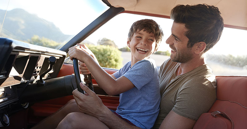Father and son looking happy while playing in car