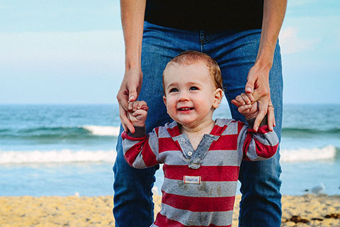 Father holding toddler boy's hands at the beach